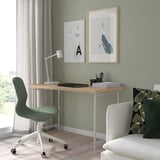 Minimalist home office with LAGKAPTEN desk, green chair, white lamp, laptop, art prints, and sofa.