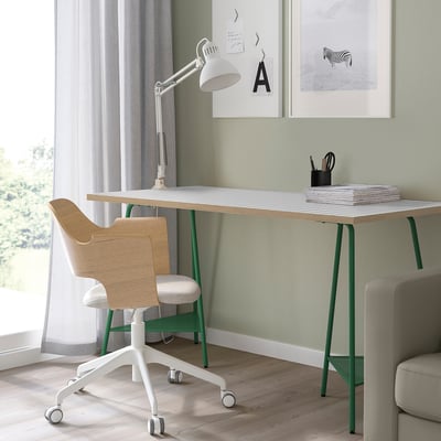 Modern home office lagkpten desk in white with green legs, wooden chair, and sleek white lamp, neatly organized with a minimalist design.