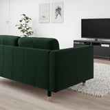 Modern living room with green sofa, tv, white rug, plant.