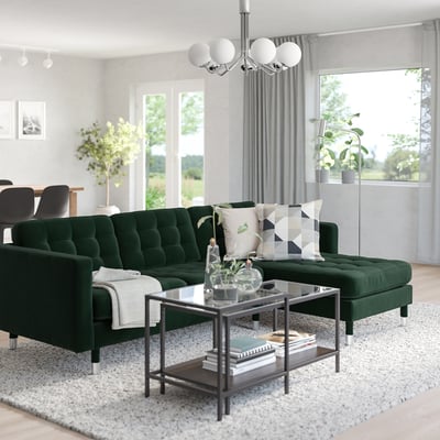Modern living room with dark green velvet sofa, chic chandelier, glass coffee table, and natural light.