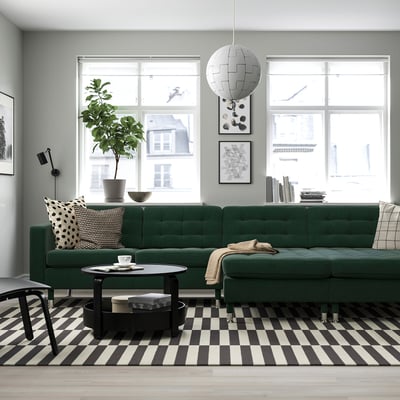 Modern living room with green velvety sofa, black-white decor, large windows.