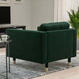 Green velvet armchair with wooden legs sits on a striped rug. Small side table holds a white mug.