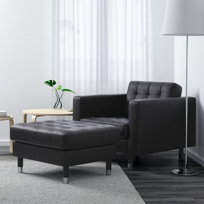 Minimalist living room: black leather chair & ottoman, wooden side table, floor lamp, plants