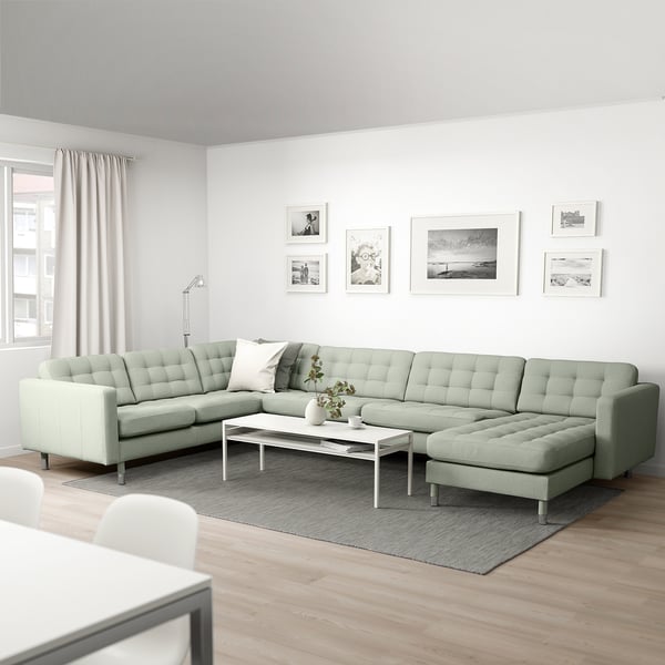 Modern living room with green l-shaped sofa, black-and-white photo wall, white coffee table, and large window.