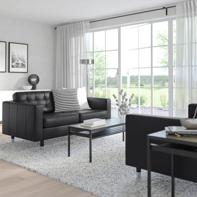 Modern living room with large window, black leather landarkrona sofa, black coffee table, white walls, and patterned rug.
