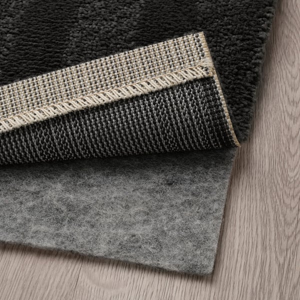 A dark grey rug with a stripe pattern is shown with a felt underside, ideal for bedroom use, providing warmth and sound dampening.