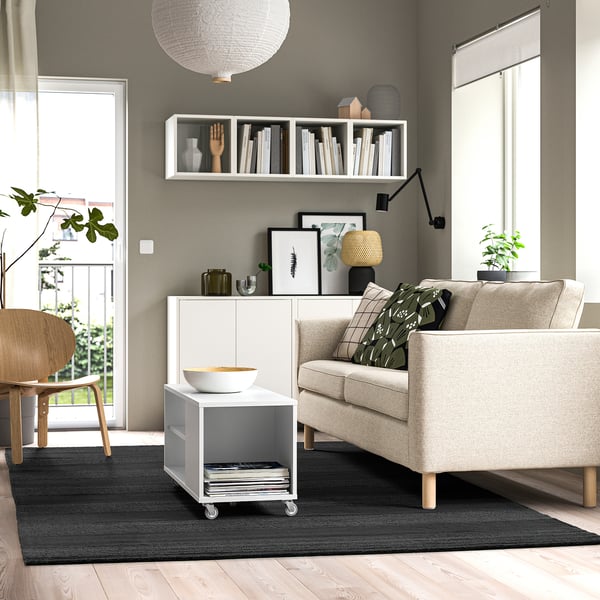 Modern living room with grey striped rug under beige sofa, complementing minimalist decor with chair, storage, and plants.