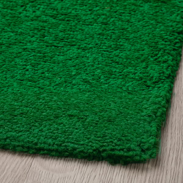 Bright green textured rug with a thick, plush pile lies on a wooden floor. Dense weave feels soft and cosy, perfect for a living space.