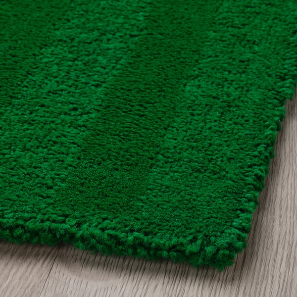 Close-up of a soft, plush, bright green rug on a wooden floor.