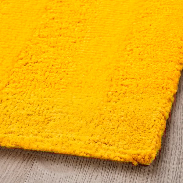 Bright yellow, textured rug with curly yarns, laying flat on a wooden floor. Soft, inviting, and appears high quality.