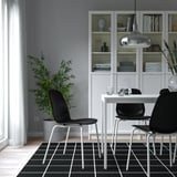 Modern dining area with black LIDÅS chairs, white table, and storage unit. Dark rug.