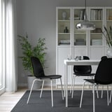 Modern dining area with white LIDÅS chairs, gray seat shells, metal legs, under hanging light, black table, bookshelves, plant, and curtained window.