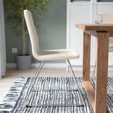 Modern beige office chair with chrome base on striped rug beside wooden table.