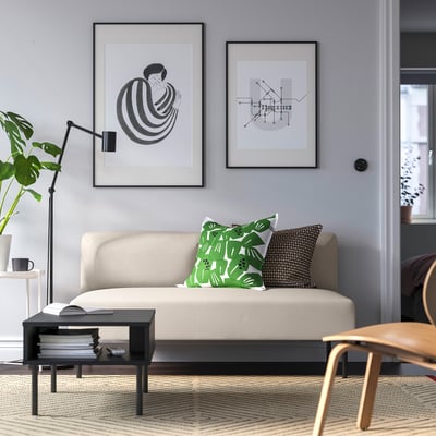 Modern living room with LILLEHEM beige sofa, green cushions, black-and-white art, black lamp, plant, coffee table, books, cup, geometric rug.