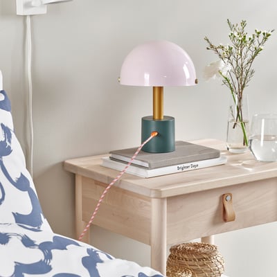 Light from LILLHULT lamp on bedside table, books, flowers, and charging cable.