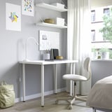Minimalist home office with white desk, shelves, lamp, notebooks, and chair. Bright space with large window and artwork.
