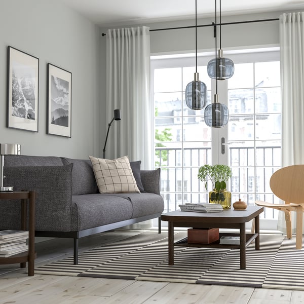 Modern living room with grey couch, striped rug, coffee table, hanging lights, city view.