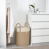 LJUNGAN beige jute laundry basket, large, with handles, near white dresser, holding clothes.