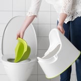 Adult places lime green and white childrens toilet seat into white toilet for training.