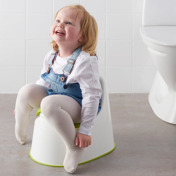 Child sits on white toilet trainer with green accents, smiling. The anti-slip base keeps it stable during use.