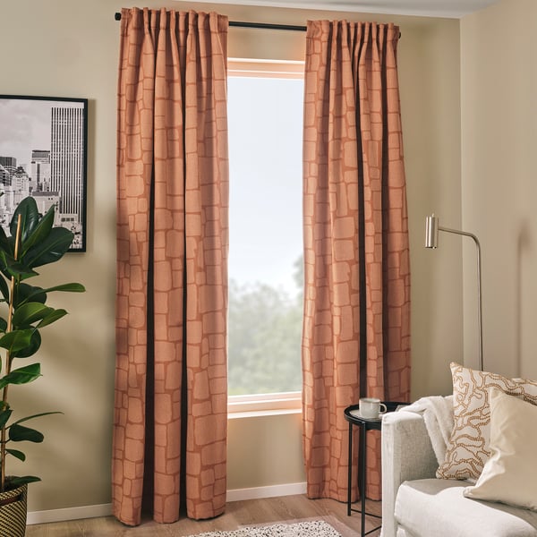 LÖNNSTÄVMAL peach curtains hang by window, darker than couch and side table, lighter than artwork.