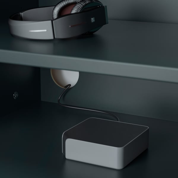 A pair of gray headphones resting on a dark surface, connected to a charging device.