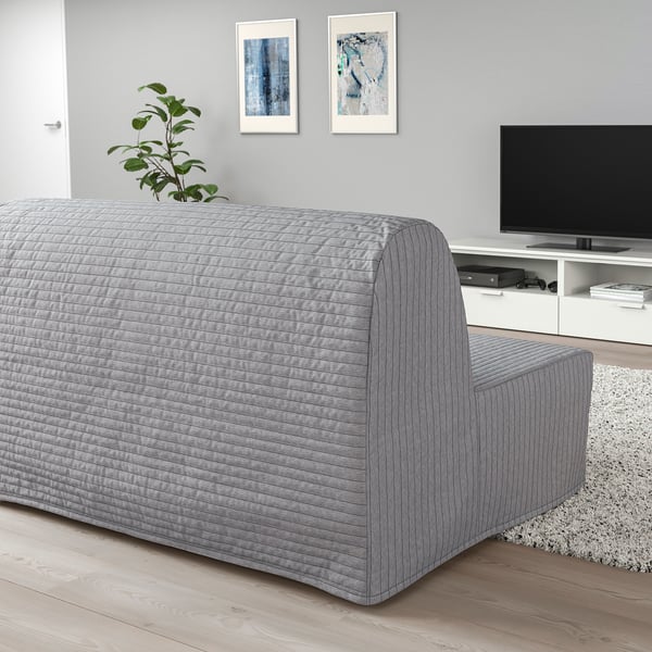 Modern gray lycksele sofa-bed in living room, beneath paintings, next to tv console, opposite door. Large, sleek, comfortable with plant on back.