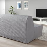 Modern gray lycksele sofa-bed in living room, beneath paintings, next to tv console, opposite door. Large, sleek, comfortable with plant on back.