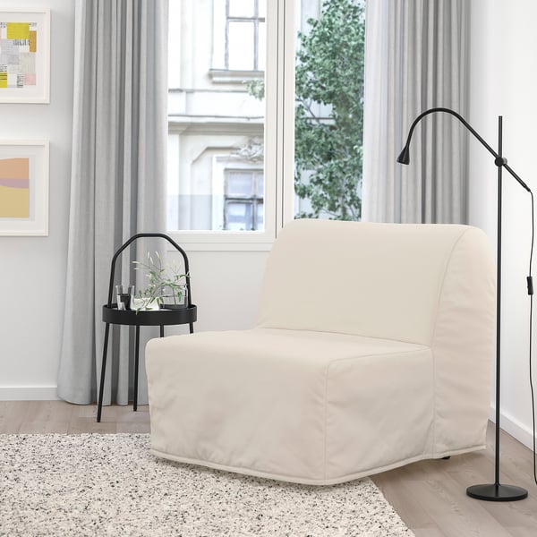 Modern minimalist living room with large white chair-bed, black side table, lamp, gray rug, and window view.
