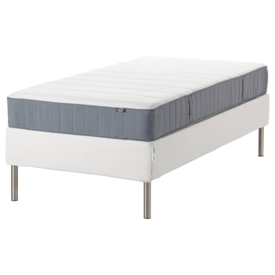 A white IKEA mattress on a white bed frame with metallic legs. It has a blue edge detail and a quilted design on top.