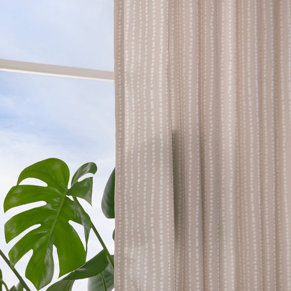Light-filtering curtains with beige and white dots hang near a large leafy plant by a window, allowing natural light while ensuring privacy.