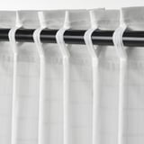 White sheer curtains with textured grid pattern hang from black rod with hooks.