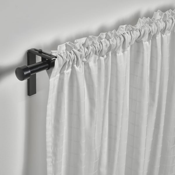 Black curtain rod holds sheer white MÄSTERROT curtains, pleated with heading tape for natural light and privacy.
