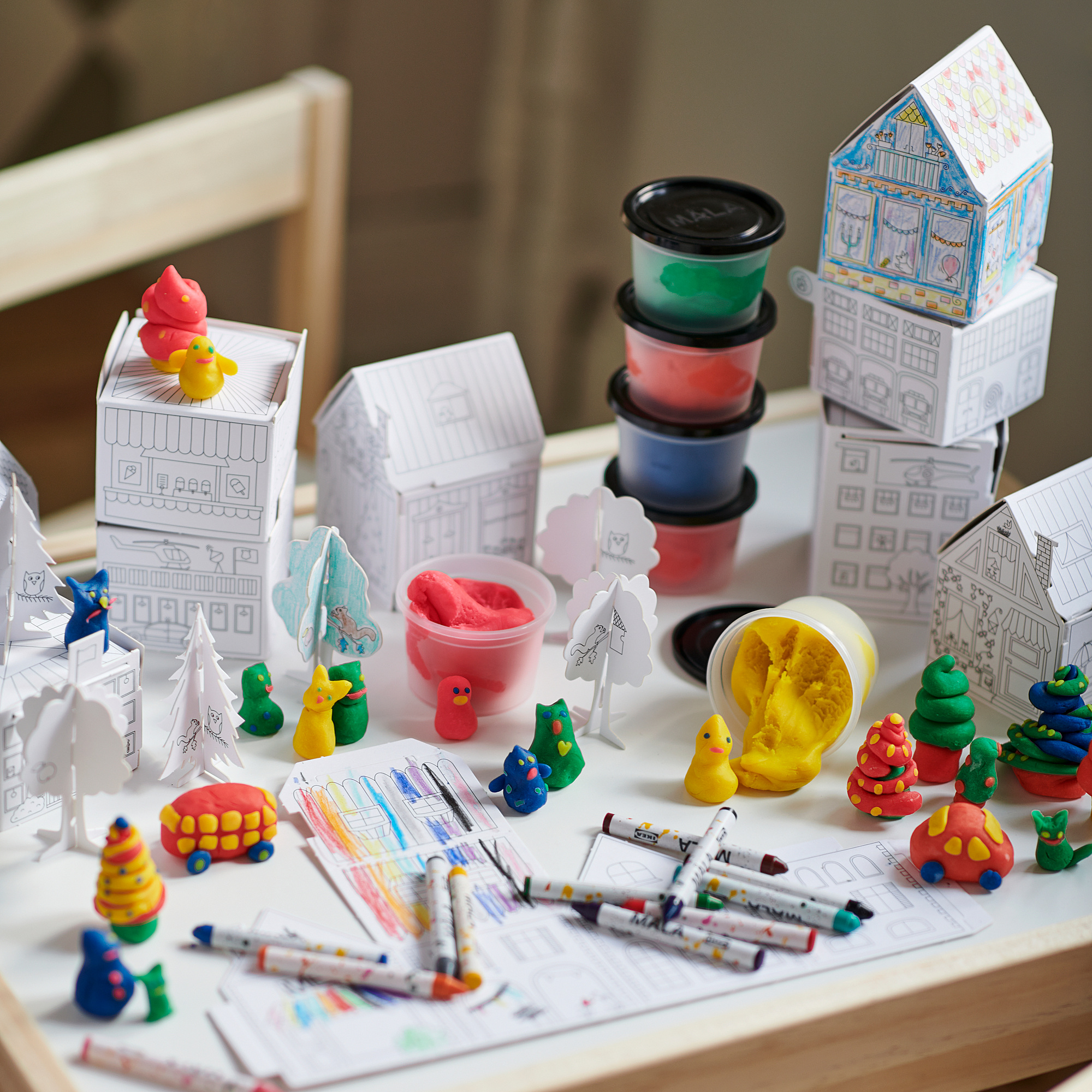 Playful scene with MÅLA craft set. Miniature houses, colorful clay, and markers on table.