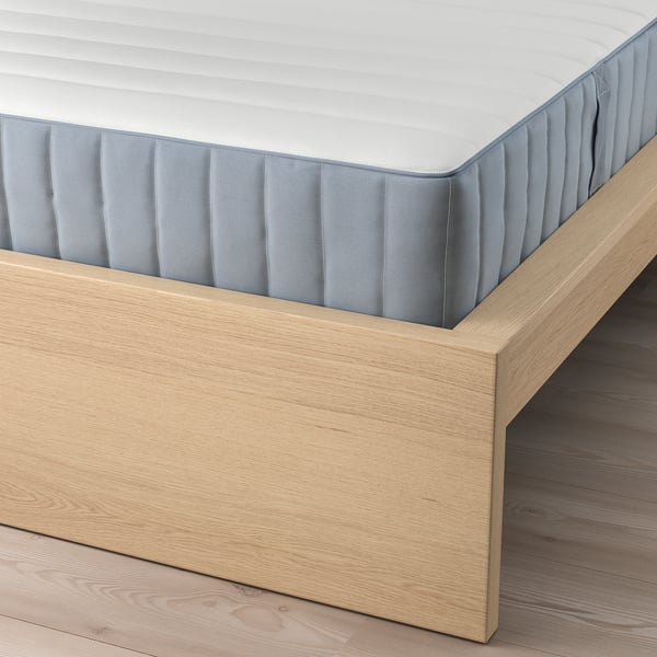 A wooden MALM bed frame with adjustable bed sides, supporting a mattress, set on a wooden floor.
