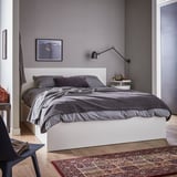 A modern gray bedroom with a MALM bed featuring dark grey linens, a white headboard, and black wall lamp.