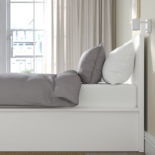 Bed with lift-up base revealing storage. Gray bedding and pillows, headboard against wall.