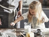 Girl and adult baking. She wears an apron, MARIATHERES.