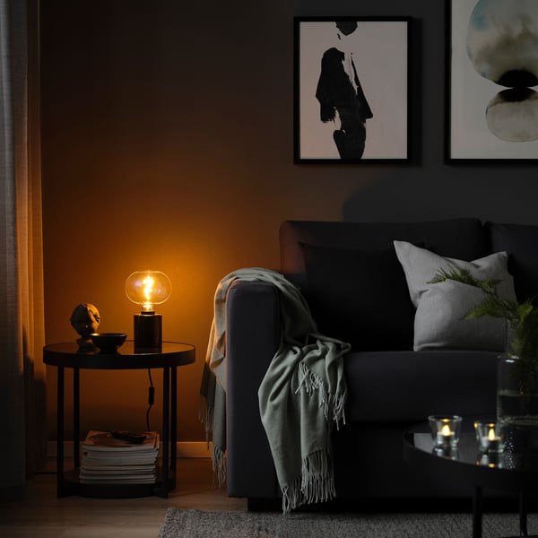 Cozy living room with lamp, couch, blanket, magazines, and abstract art.