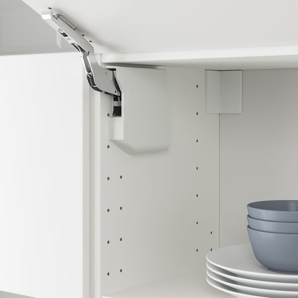 White kitchen cabinet with door lift hinge, gently closing mechanism, and stack of blue bowls and white plates.