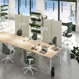 Modern office setup with MITTZON beige tables, green chairs, and high dividers. Laptops and lamps on tables, large windows in background.