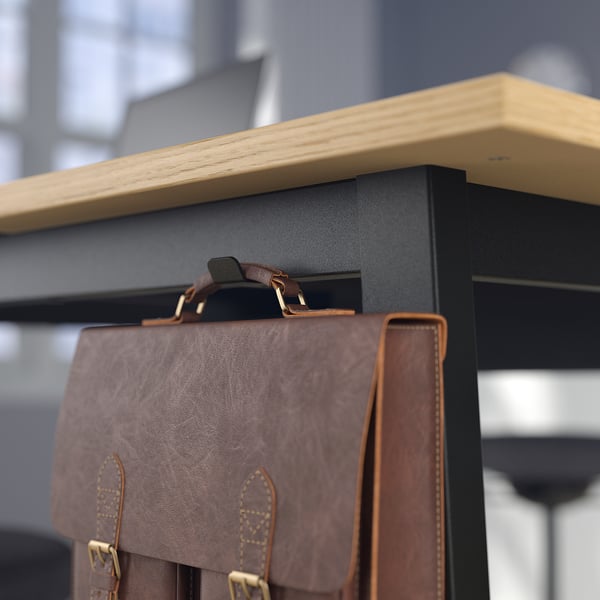 Brown leather bag hangs on black metal hook, linked to wooden shelf, fitting office decor.
