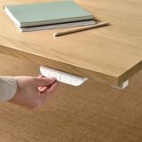 Adjustable desk with hand control. Person operates electric sit/stand mechanism, next to books and pencil.