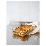 Clear glass oven dish with golden-brown baked food. Used on a white surface. Suitable for microwave, oven, and dishwasher.