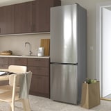 Modern kitchen with large stainless steel MÖLNÅS fridge. Brown cabinets, wooden chair, countertop items, and grocery bag.