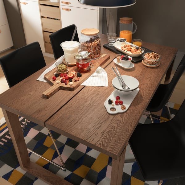 Modern kitchen with oak table and black chairs, breakfast items on wooden table.