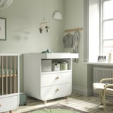 White changing table, wooden crib, hanger with clothes, baby mobile, striped rug, green walls.