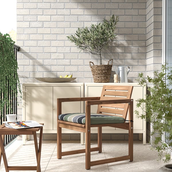 Modern balcony scene: light beige NÄMMARÖ chair, striped cushion, side table, cabinet, and potted plant against light brick wall.