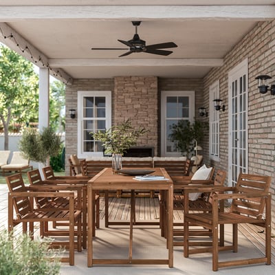 Outdoor dining set with table, chairs, & fan. Brick building backdrop with plants. Bright & inviting.