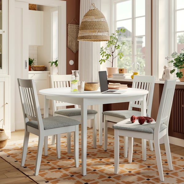 NÄSINGE white round dining table with 4 chairs, grey cushioned seats, solid wood legs, placed on a patterned rug near a window.